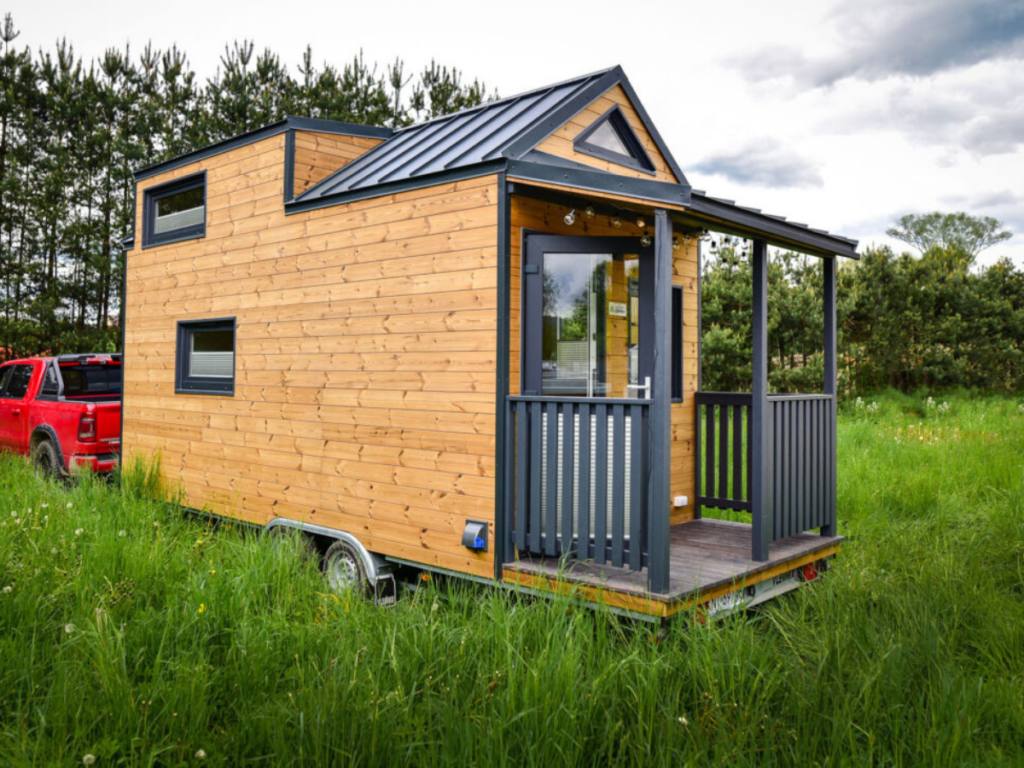 A glamping structure - a tiny house sitting on a trailer in a grassy field.