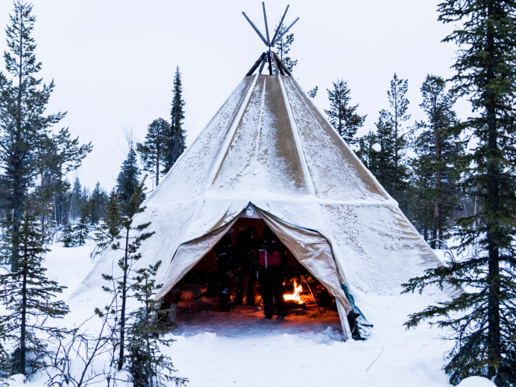 A glamping teepee nestled in the snowy wilderness, adorned with a crackling fire to keep you warm.