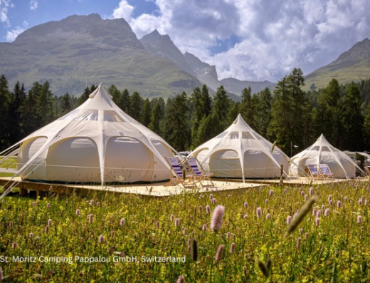 Luxury glamping tents set up in a lush meadow with alpine mountains in the background in st. moritz, switzerland.
